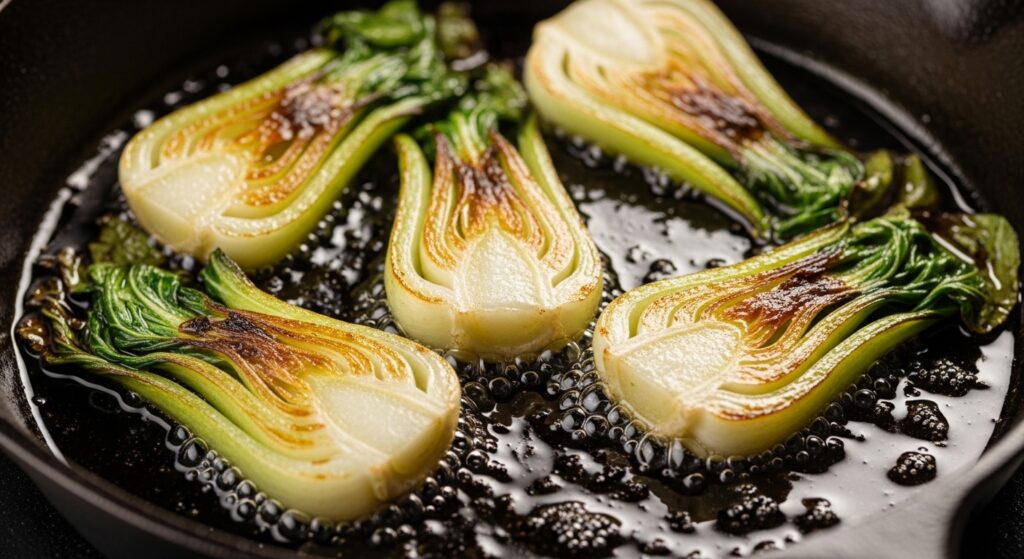 Baby bok choy searing in a skillet to achieve golden caramelization.